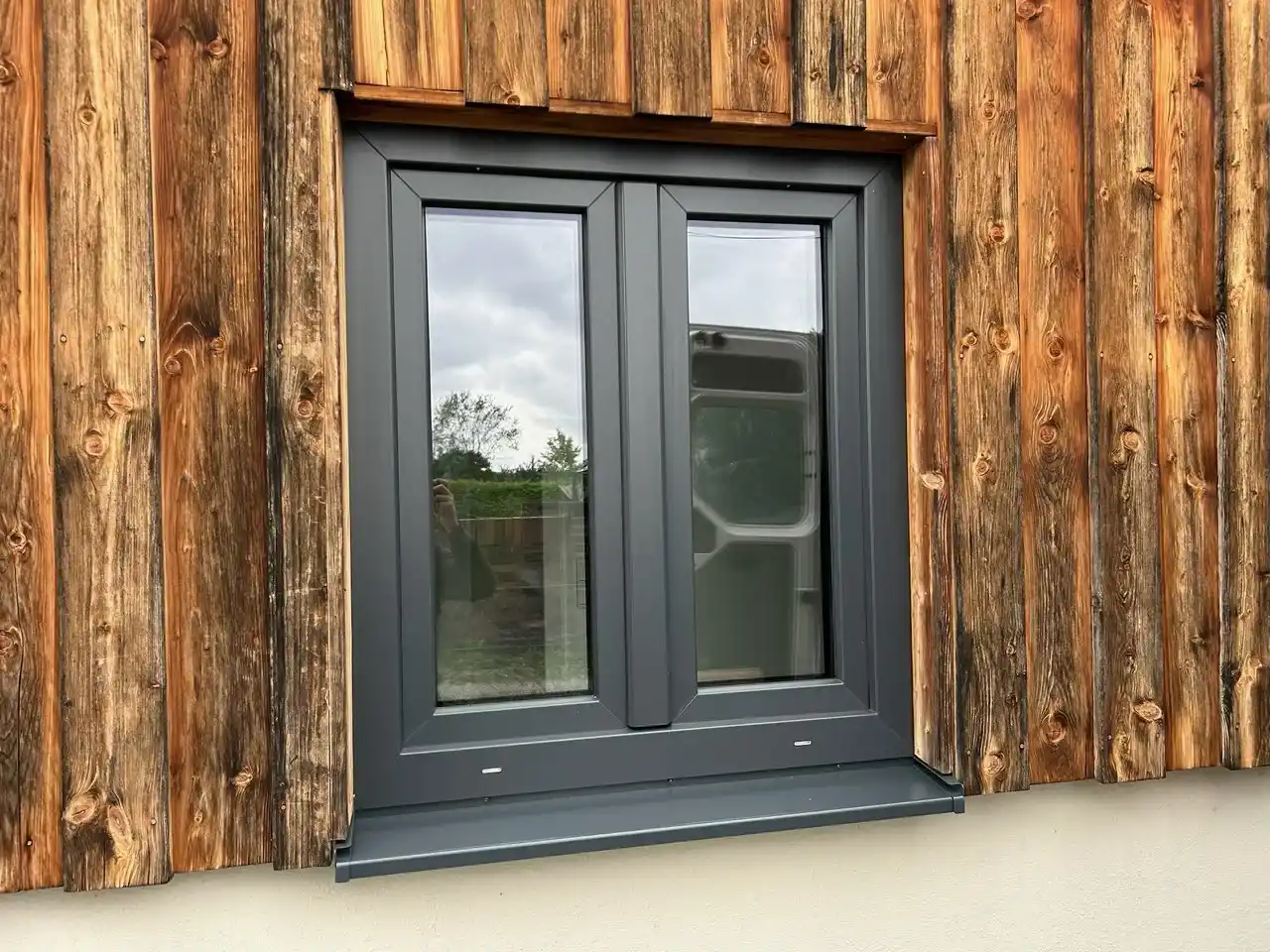Zweiflügeliges Fenster mit anthrazitfarbenem Rahmen in einer Fassade aus senkrechten Holzbrettern